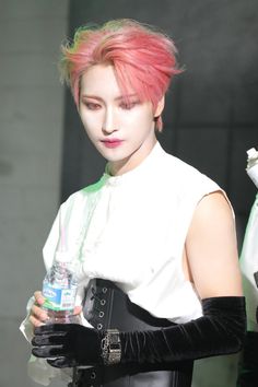a woman with pink hair and black gloves holding a water bottle in her right hand