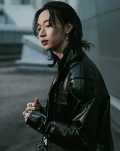 a woman in black leather jacket standing on the street with her hand up to her chest