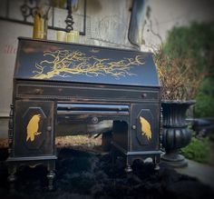an old fashioned desk with gold designs on the top and bottom, sitting in front of a building