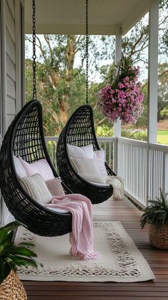 two black hanging chairs on a porch with pink and white pillows, one is empty