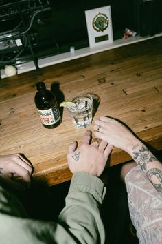 two people sitting at a wooden table with drinks in front of them and one holding the other's hand