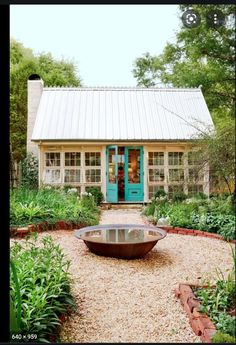 a small house with a blue door in the middle of a gravel path and lots of greenery
