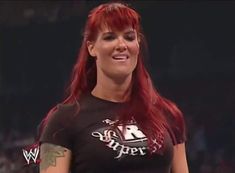 a woman with long red hair and tattoos on her chest smiles at the camera while standing in front of an audience