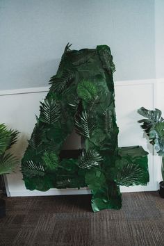 there is a green letter made out of leaves on the floor next to some plants