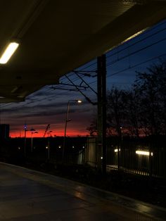 an empty bus stop at night with the sun setting in the distance and lights on
