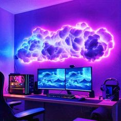 two computer monitors sitting on top of a desk in front of a neon cloud wall