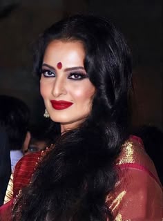 a woman with long black hair and red lipstick wearing a gold sari, posing for the camera