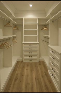 an empty walk in closet with white drawers and wooden flooring is seen here, while the light shines on the shelves