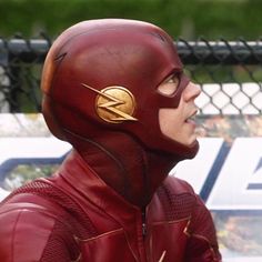 a man in a flash costume standing next to a chain link fence and looking off into the distance