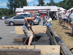 a man is digging into some wood in the parking lot while people watch from behind him