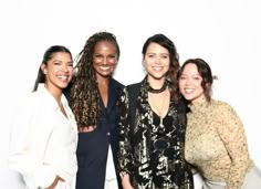 four women posing for a photo together in front of a white background with one woman smiling at the camera
