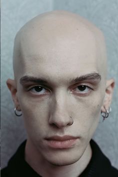 a bald man with piercings on his ears and nose is looking at the camera