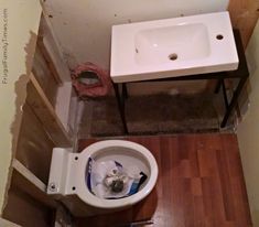 a white toilet sitting next to a sink in a bathroom under construction with wood flooring