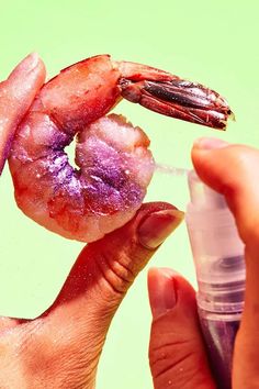 a hand holding a small bottle filled with pink and purple substance next to a shrimp