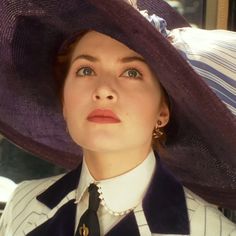 a woman wearing a large purple hat and striped dress shirt, with her eyes wide open