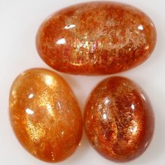 three shiny orange rocks sitting next to each other on a white surface with gold flecks