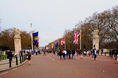 many people are walking down the street with flags on poles in front of some trees