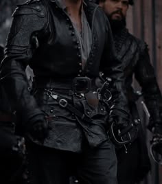 two men dressed in black and one wearing a leather outfit, both with gloves on