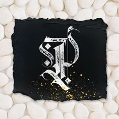 a black stone with white rocks surrounding it and the letter s painted on it, surrounded by gold sprinkles