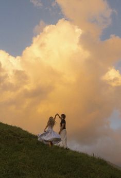 two women standing on top of a lush green hillside under a cloudy sky with clouds