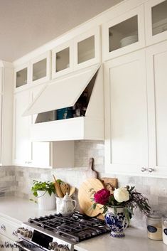 a kitchen with white cabinets and marble counter tops, including an oven hood over the stove