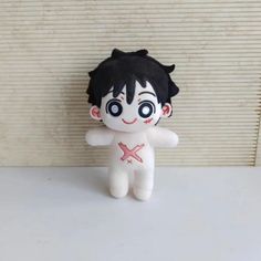 a stuffed animal doll with black hair and big eyes sitting on a white surface next to a wall
