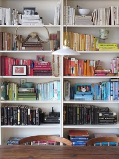 a bookshelf filled with lots of books next to a wooden table and chairs