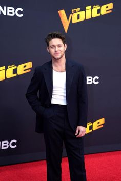 a man in a black suit and white shirt standing on a red carpet with his hands in his pockets
