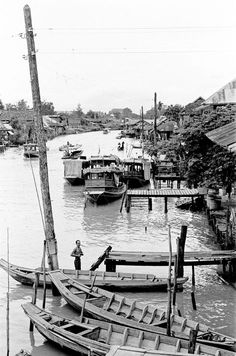 an old black and white photo of several boats in the water near houses on stilts