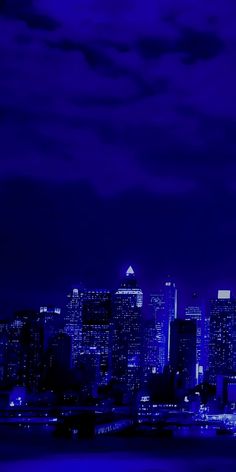 the city skyline is lit up at night with bright blue lights and clouds in the sky