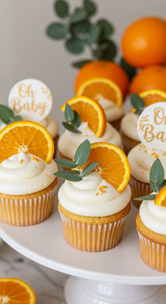 cupcakes decorated with orange slices and greenery on a white cake platter