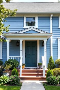 a blue house with white trim and steps leading up to the front door that is flanked by bushes