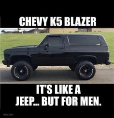 a black truck parked on top of a parking lot next to a grass covered field