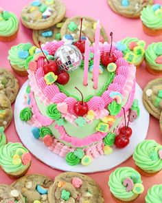 a birthday cake surrounded by cupcakes and cookies on a pink table with candles