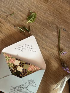 an open envelope sitting on top of a wooden table next to some flowers and writing