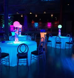 an empty banquet room with round tables and chairs lit up by colorful lights at night