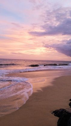 the sun is setting over the ocean with waves coming in to shore and rocks on the beach