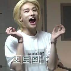 a young man with blonde hair is laughing and holding his hands in the air