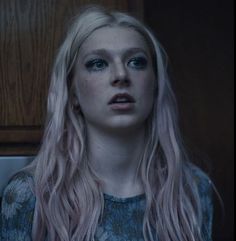 a woman with long blonde hair standing in front of a microwave oven and looking at the camera