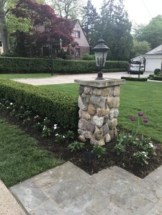 a stone pillar sitting in the middle of a garden next to a lush green lawn