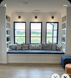 a window seat with pillows on it in front of two large windows and bookshelves
