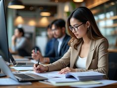 a woman sitting at a desk in front of a computer and writing on a piece of paper