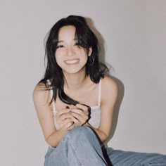 a woman sitting on the floor with her legs crossed and wearing jeans, smiling at the camera