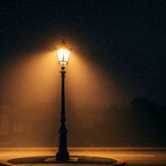 a street lamp lit up at night with stars in the sky behind it and fog on the ground