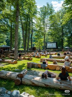 people sitting on logs in the middle of a park with trees and a projector screen