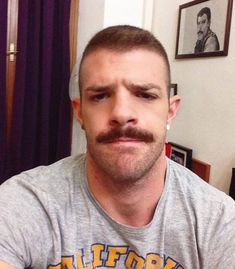 a man with a mustache is looking at the camera while wearing a t - shirt