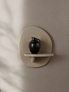 a black vase sitting on top of a white shelf next to a wall mounted shelf