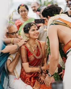 a woman in a red and gold sari smiles as she is surrounded by other people