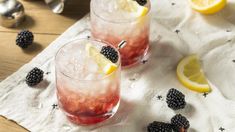 two glasses filled with blackberries and lemonade sitting on top of a white cloth