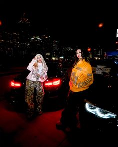 two people standing in front of a car at night, one wearing a yellow jacket